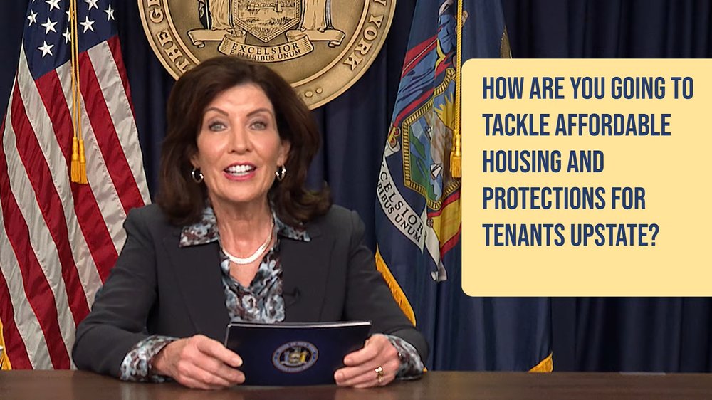 Governor Kathy Hochul holds cards and appears with a yellow text box that reads "how are you going to tackle affordable housing and protections for tenants upstate"?