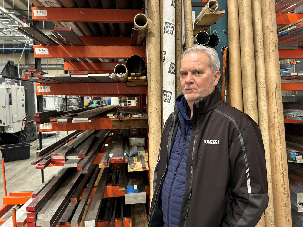 A man stands in front of pipes and other materials in a factory.