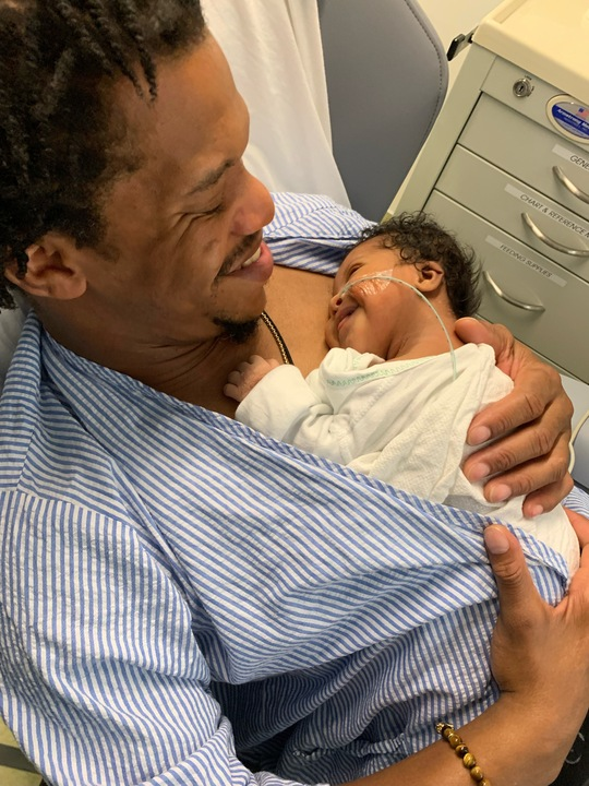 A father holds a smiling baby boy with an oxygen tube going into his nose.