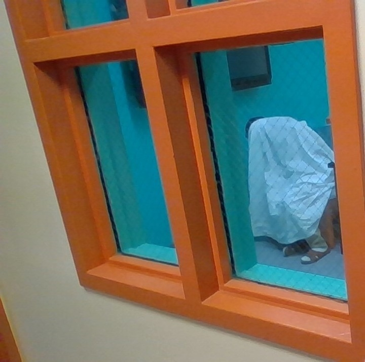 A photo taken in June, 2023 of a teen, seen through a window, sitting on a chair with a sheet over his head.