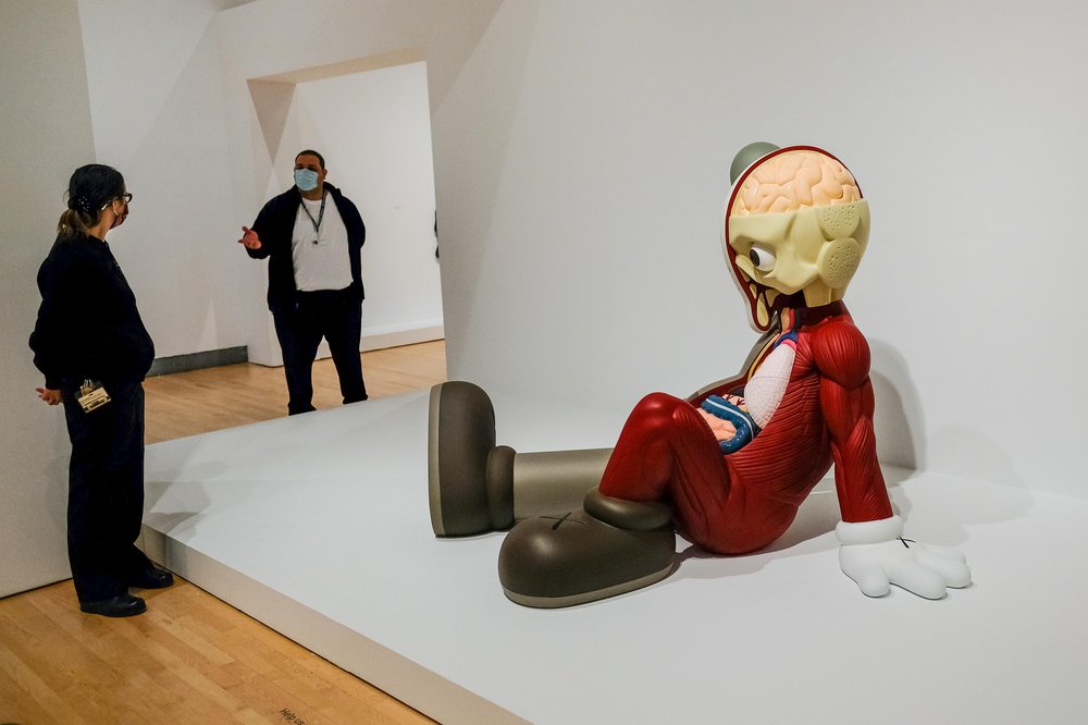 KAWS Brooklyn Museum Sculpture of figure sitting on floor. Inside the KAWS exhibit at Brooklyn Museum