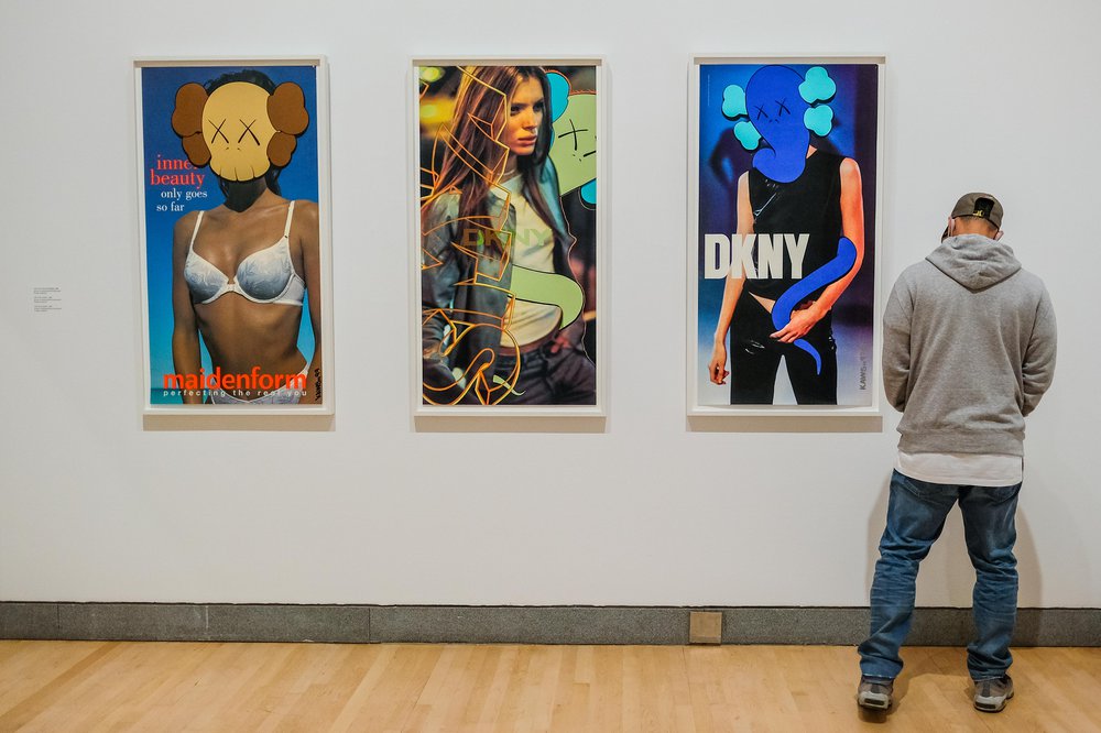 KAWS Brooklyn Museum Man looking at 3 pieces hanging on the wall. Inside the KAWS exhibit at Brooklyn Museum