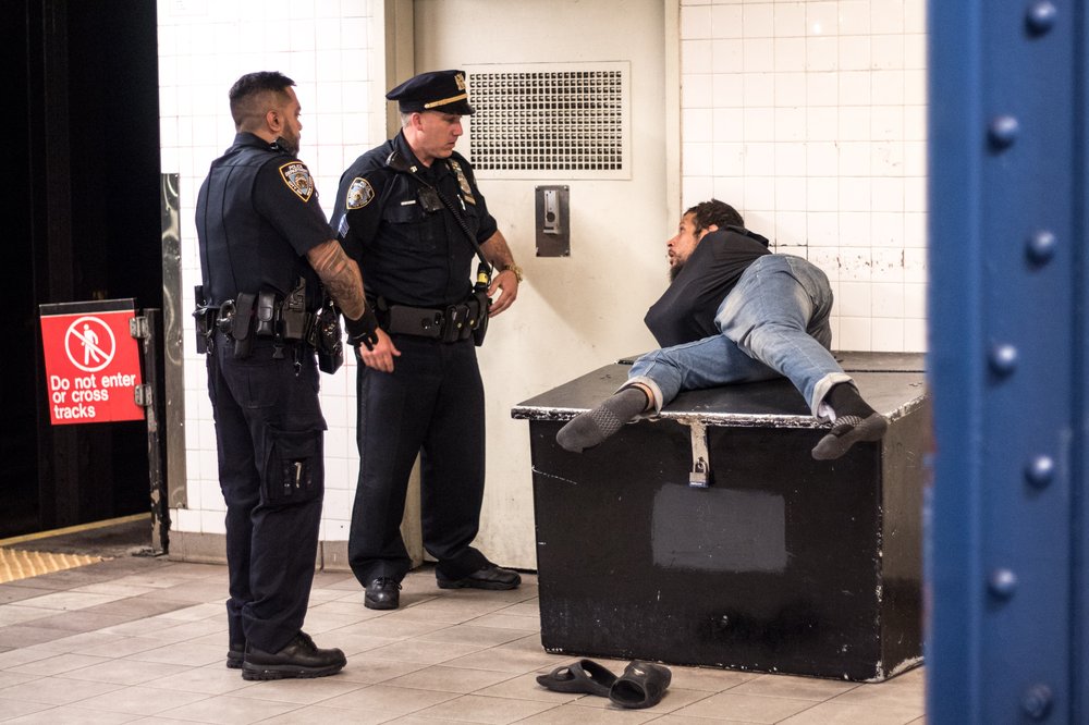 Man sleeping in subway awoken by two NYPD officers on Aug. 23, 2019. NYC policy now allows forcible removal of people who can't meet their basic needs, even when social workers and mental health professionals aren't around to assess the situation.