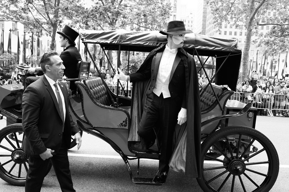A man dressed as the Phantom of the Opera stands on a carriage.