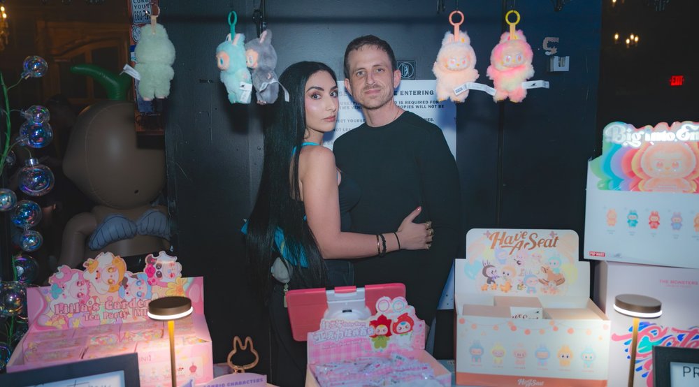 A man and a woman pose in front of Labubu merchandise.