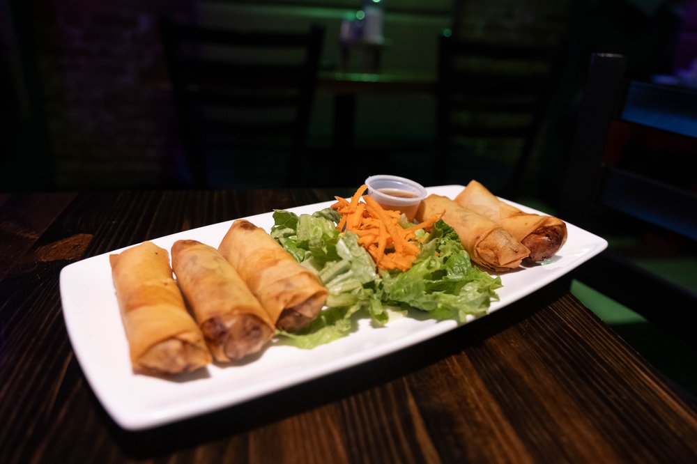 A white plate of nems, or spring rolls, with a small salad in the center