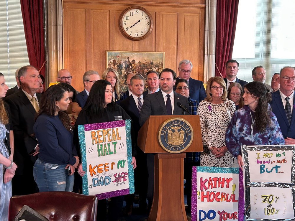 People gathered around a podium with signs opposing HALT, a law to restrict the use of solitary confinement