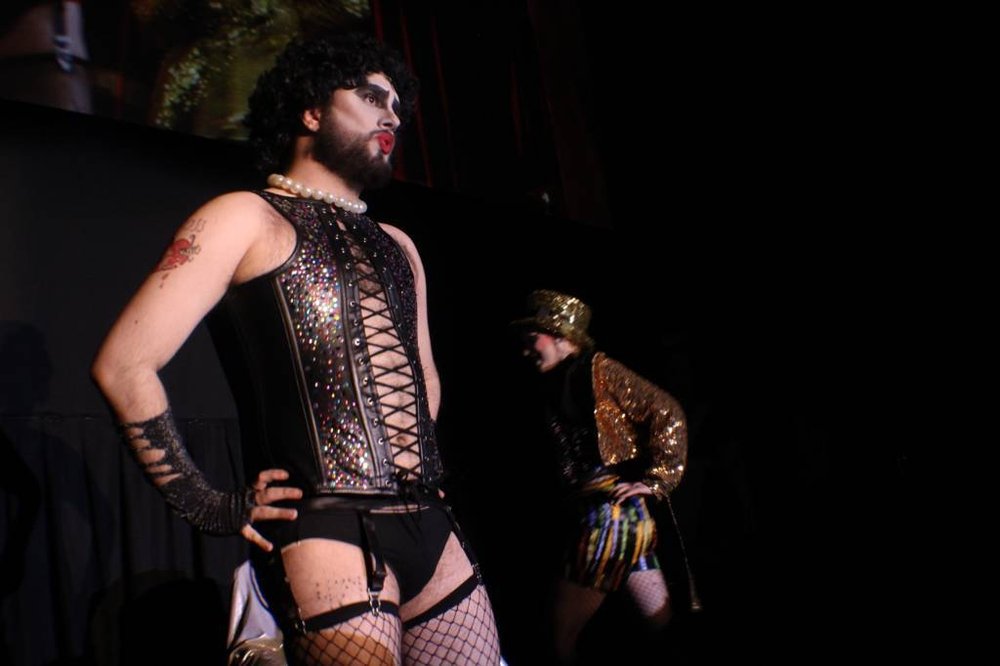 A man in a corset stares at the audience.