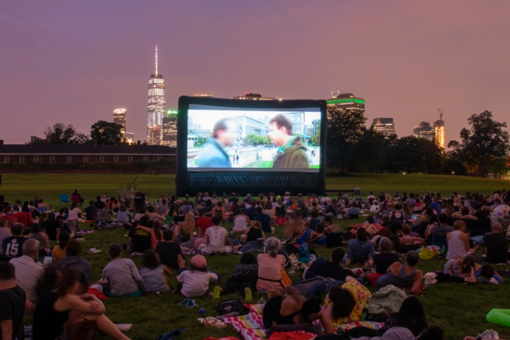 A crowd of people watching a film on an outdoor screen.