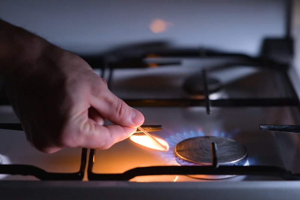 A man's hand lights a gas stove with a match.