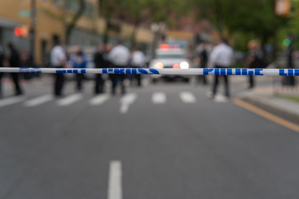 Police tape in the foreground with a police vehicle in the background, blurred