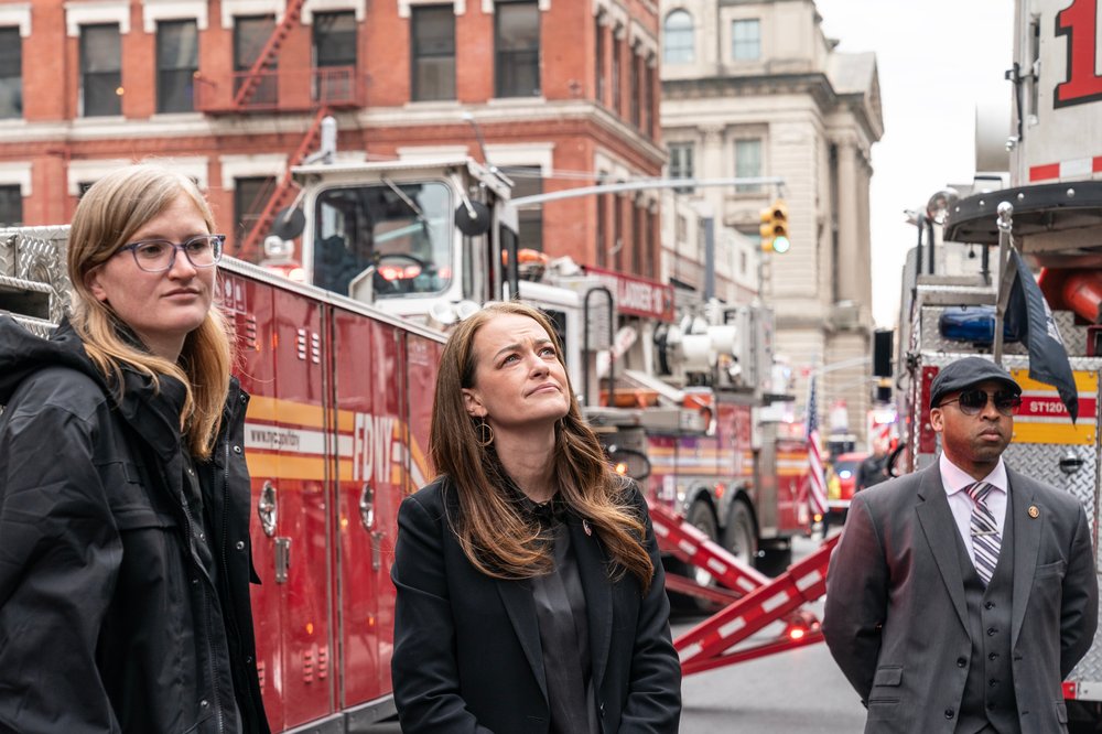 Several people look on as fire trucks are parked in the background.