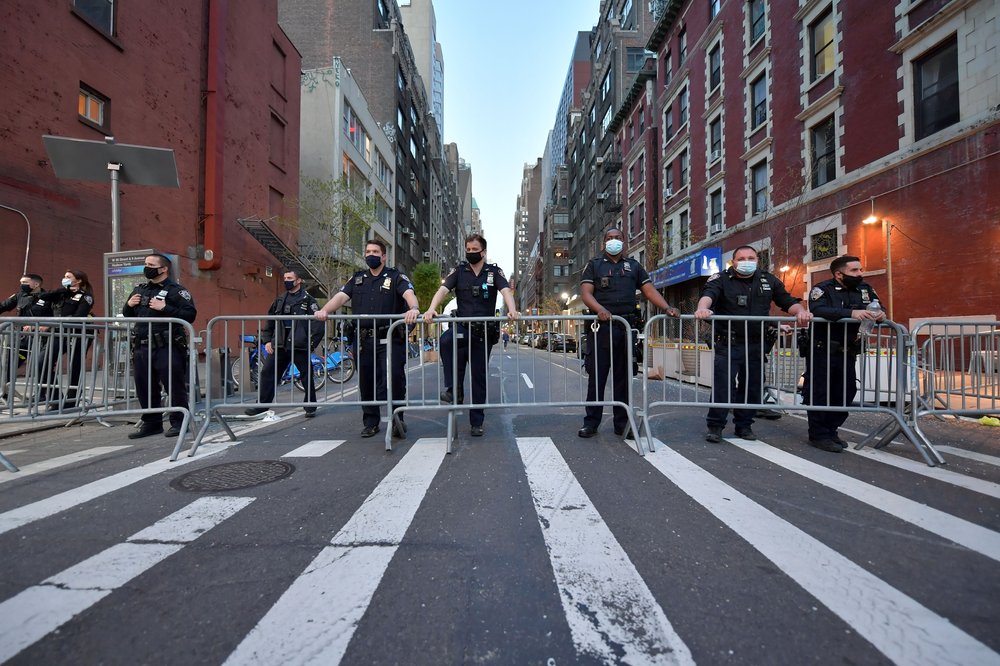 A line of police officers stand behind a metal NYPD fence.