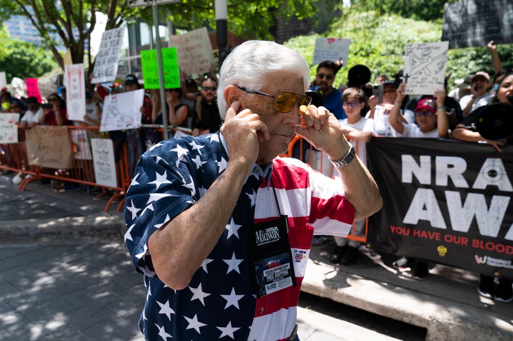 Member of the National Rifle Association plugs his ears with his fingers as he walks past protesters during the NRA's annual meeting at the George R. Brown Convention Center in Houston on May 27, 2022, just days after a gunman killed 21 people at a school in Uvalde, Texas.