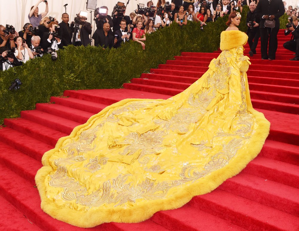 The yellow coat is dramatically trailing behind Rihanna on the red carpeted steps outside the Metropolitan Museum of Art.