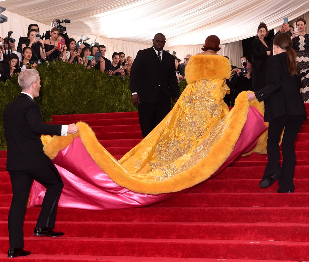 Rihanna's heavy yellow train has a pink lining, as handlers hold it up as she acends up the stairs at the 2015 Met Gala