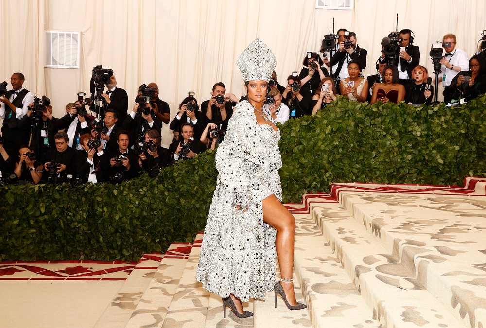 Rihanna in a silver and white Pope-inspired outfit of short mini dress, elaborate coat, and mitre hat