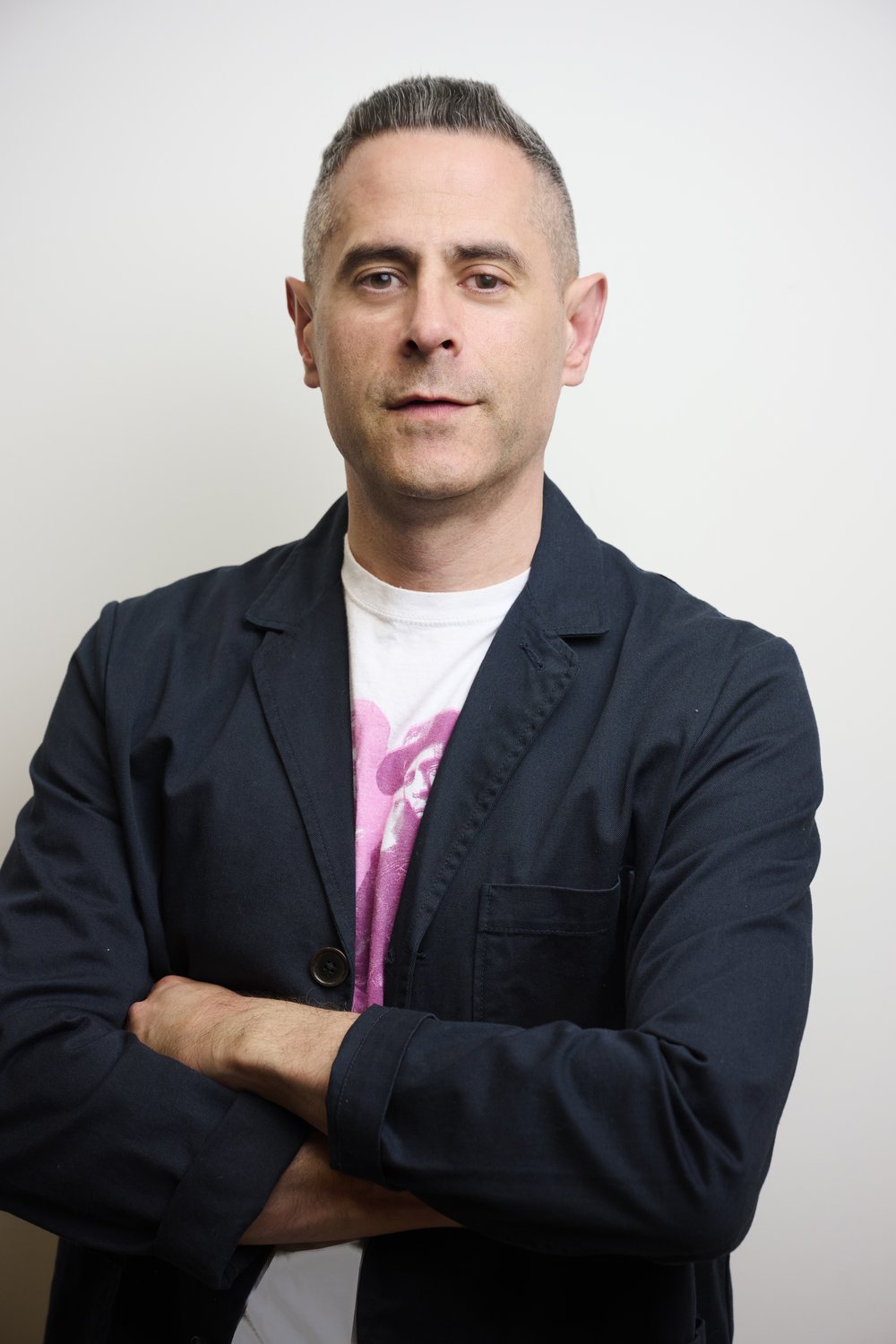 A headshot of a man shot from the waist up with his arms crossed, wearing a blazer.