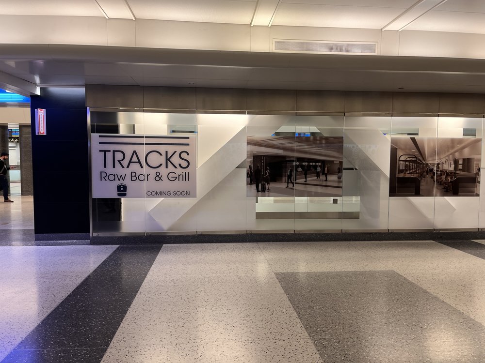 a "coming soon" sign on glass near the future location of Grand Central Madison's Tracks Raw Bar and Grill