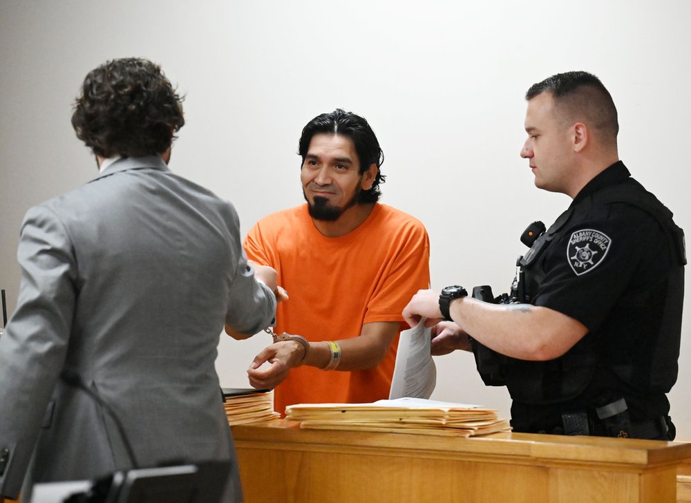 A man in a orange jumpsuit in court.