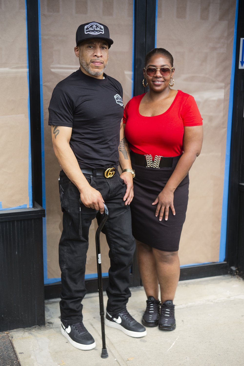 Two people stand side-by-side in front if glass doors with brown paper in the windows.