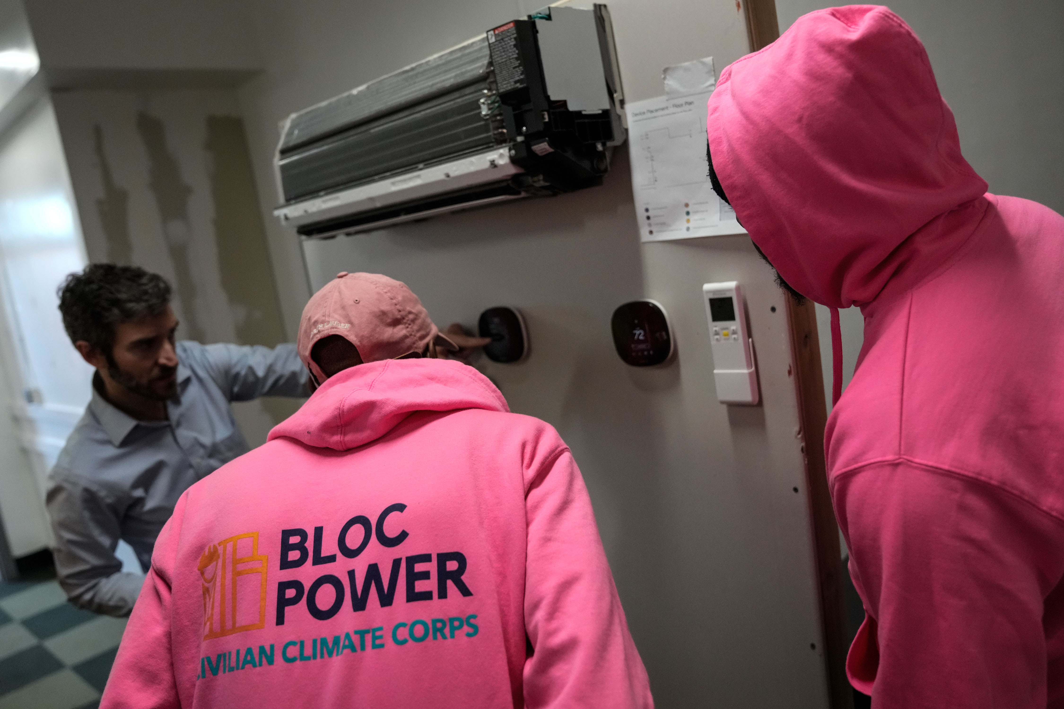 A man in a "civilian climate corps" hoodie examines a heat pump.