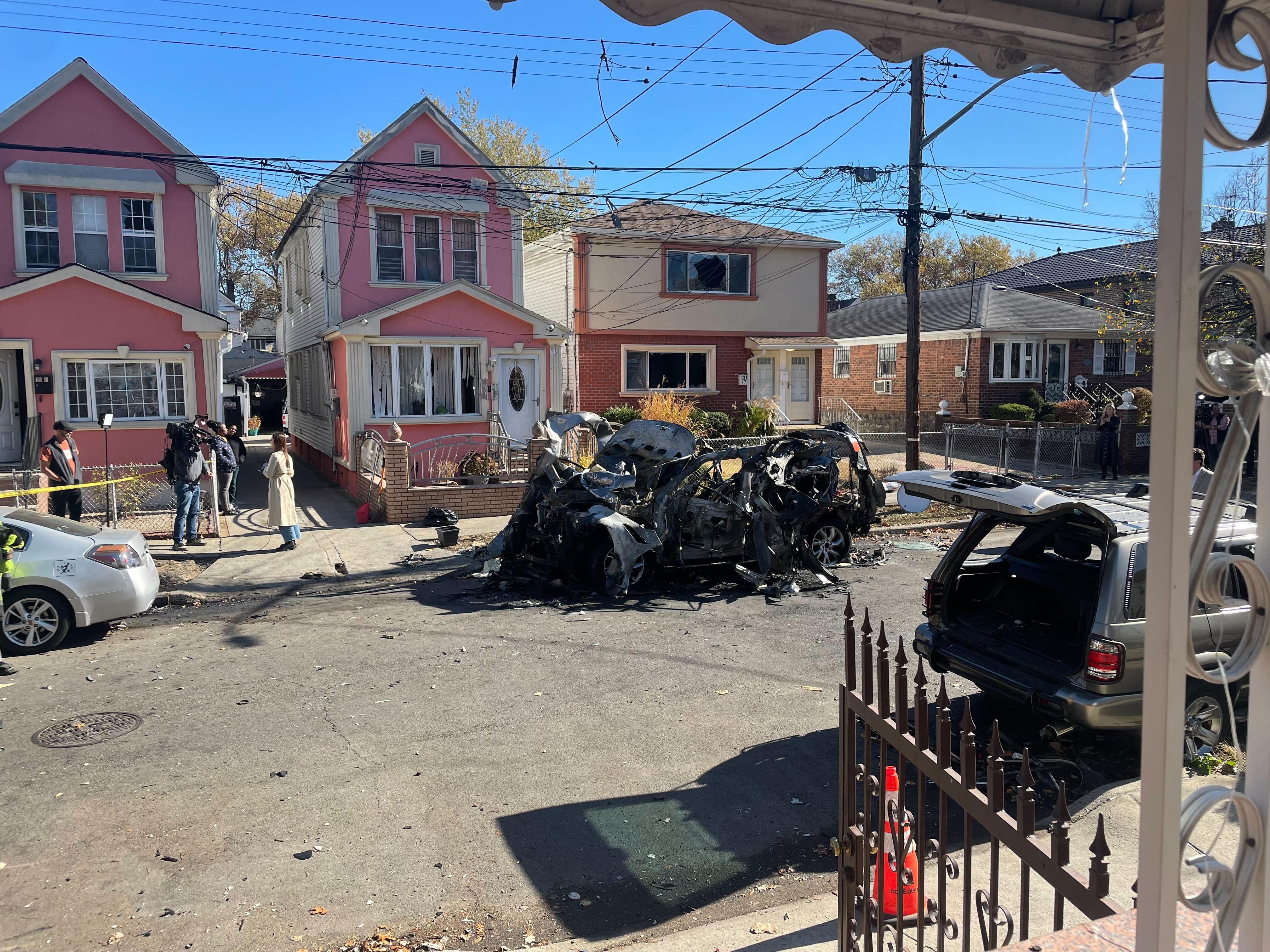 A photo of the mangled wreckage of a car that exploded in Queens and the houses it damaged.