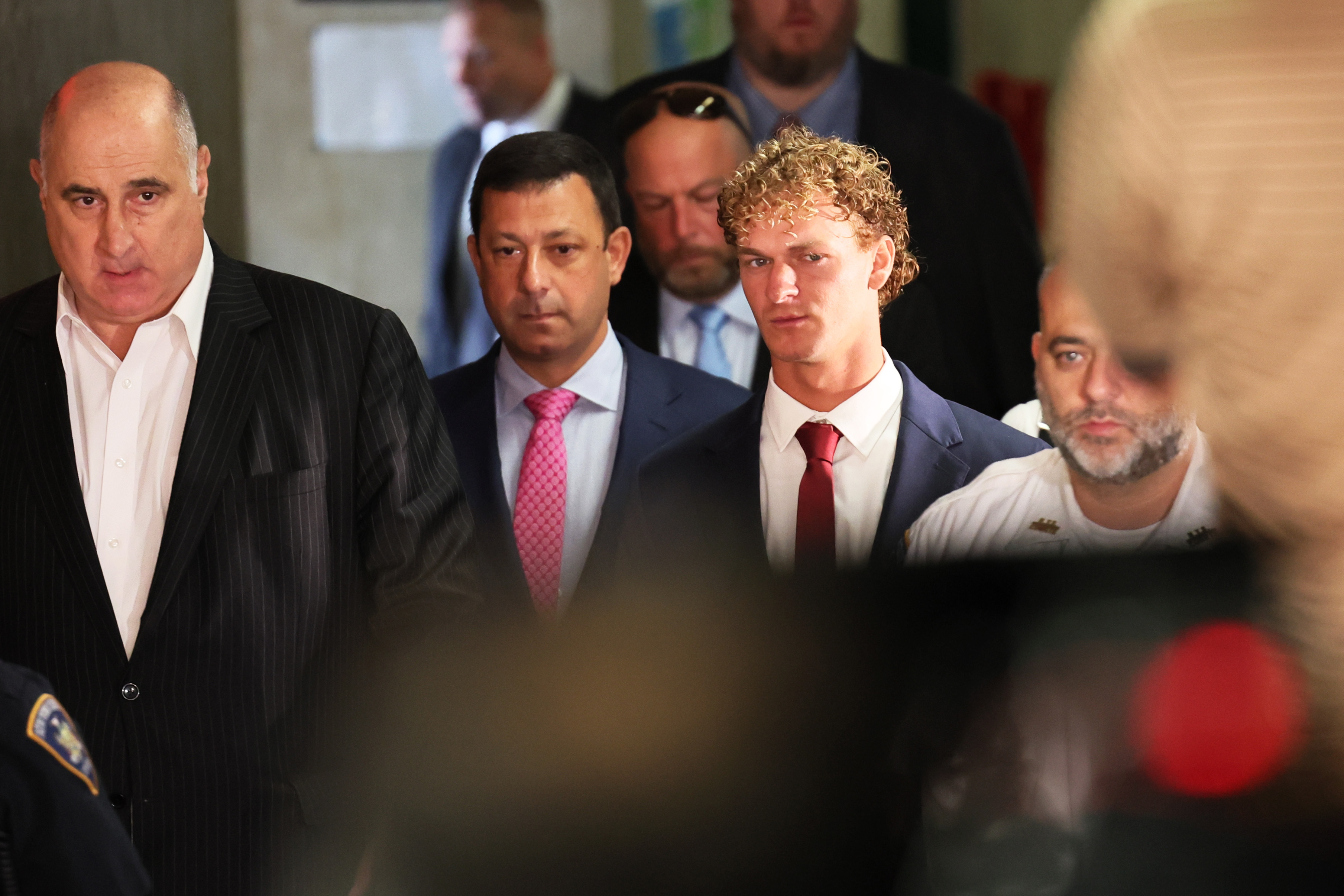 Three men in suits walk through a courthouse. At right is Daniel Penny, arriving for an arraignment hearing, on June 28, 2023.