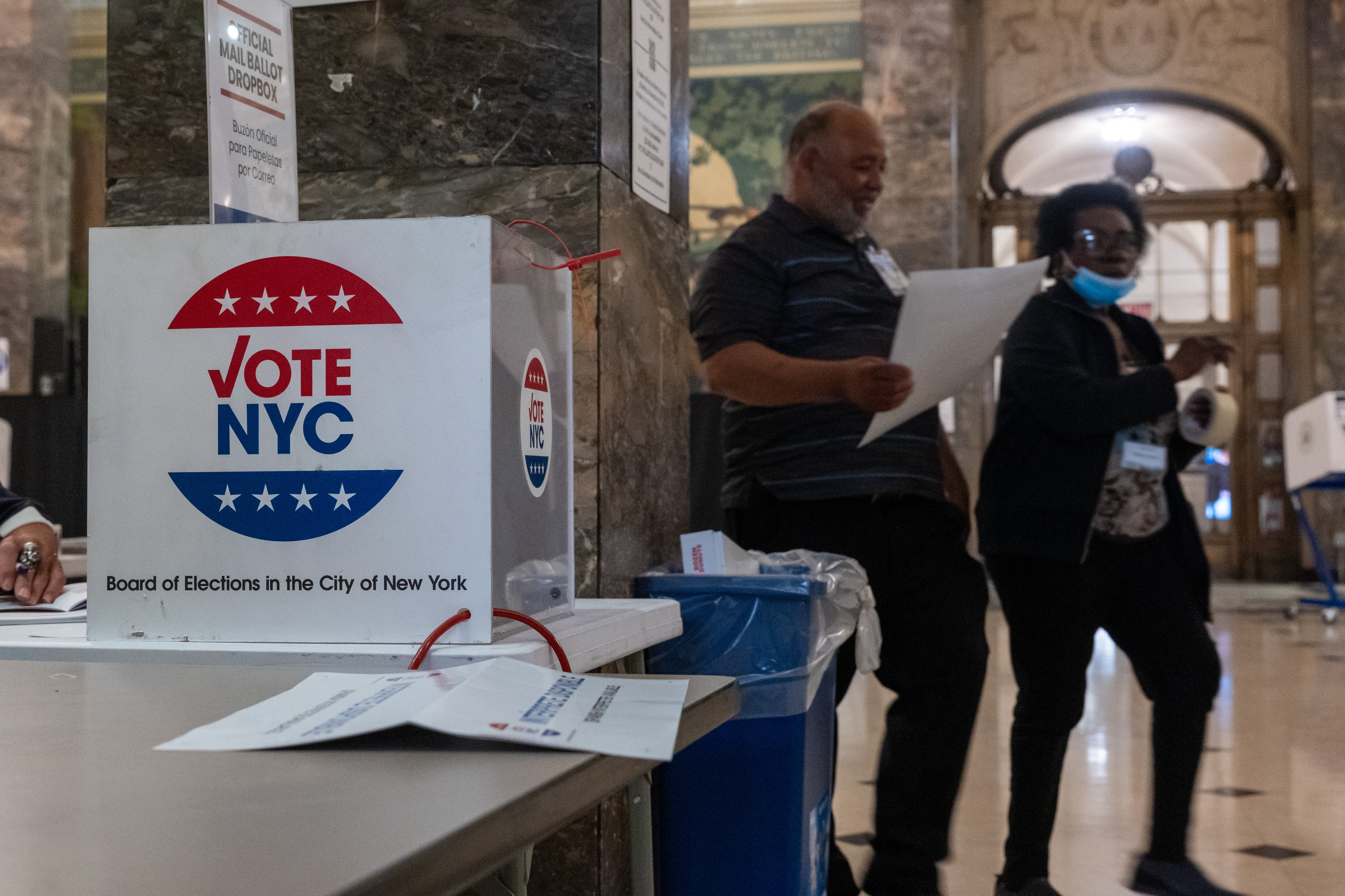 A sign says "VOTE HERE" in a courthouse with people standing nearby