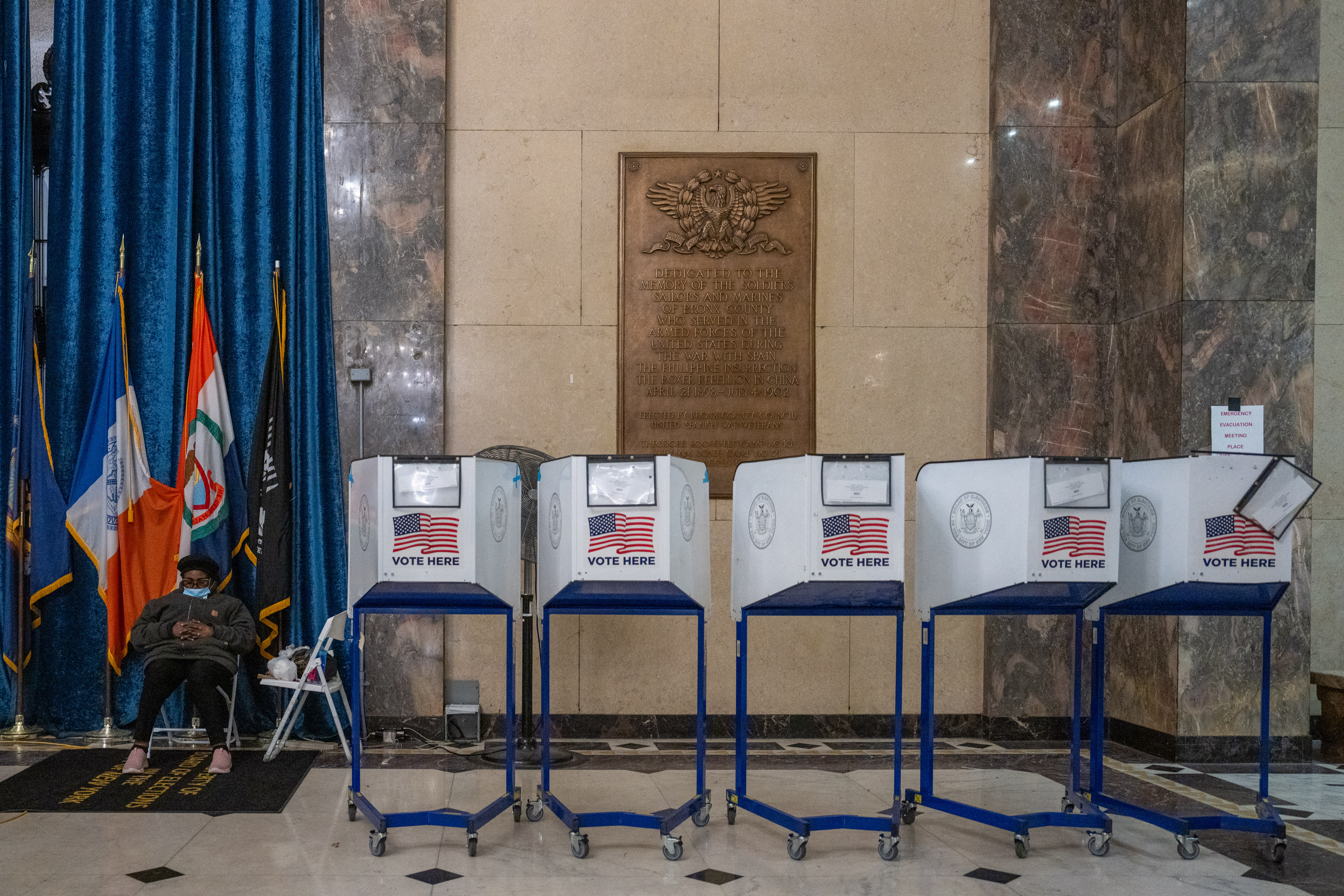 One person sits on a chair next to four empty voting booths.