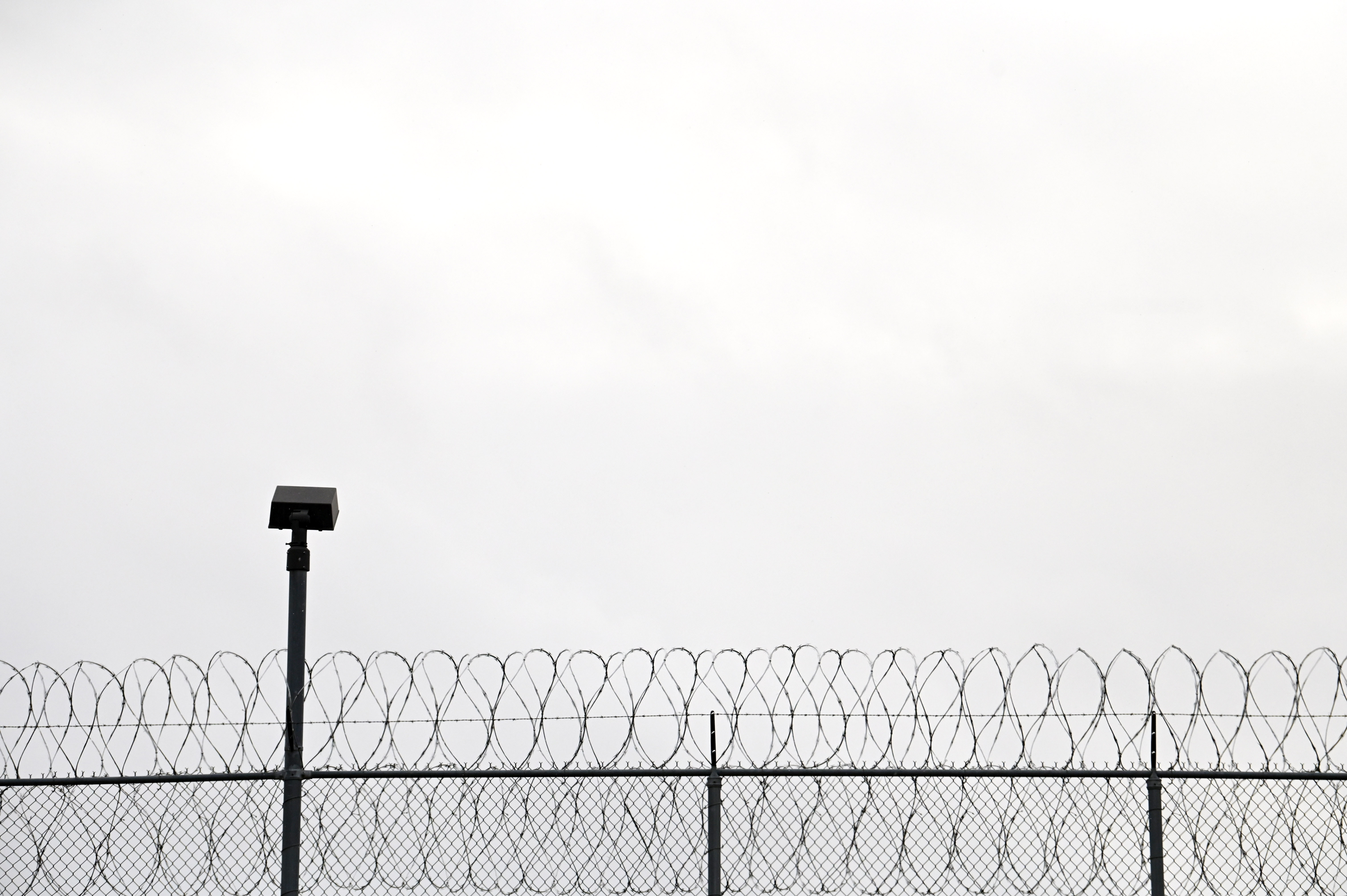 Barbed wire against a gray sky with a surveillance camera to the left