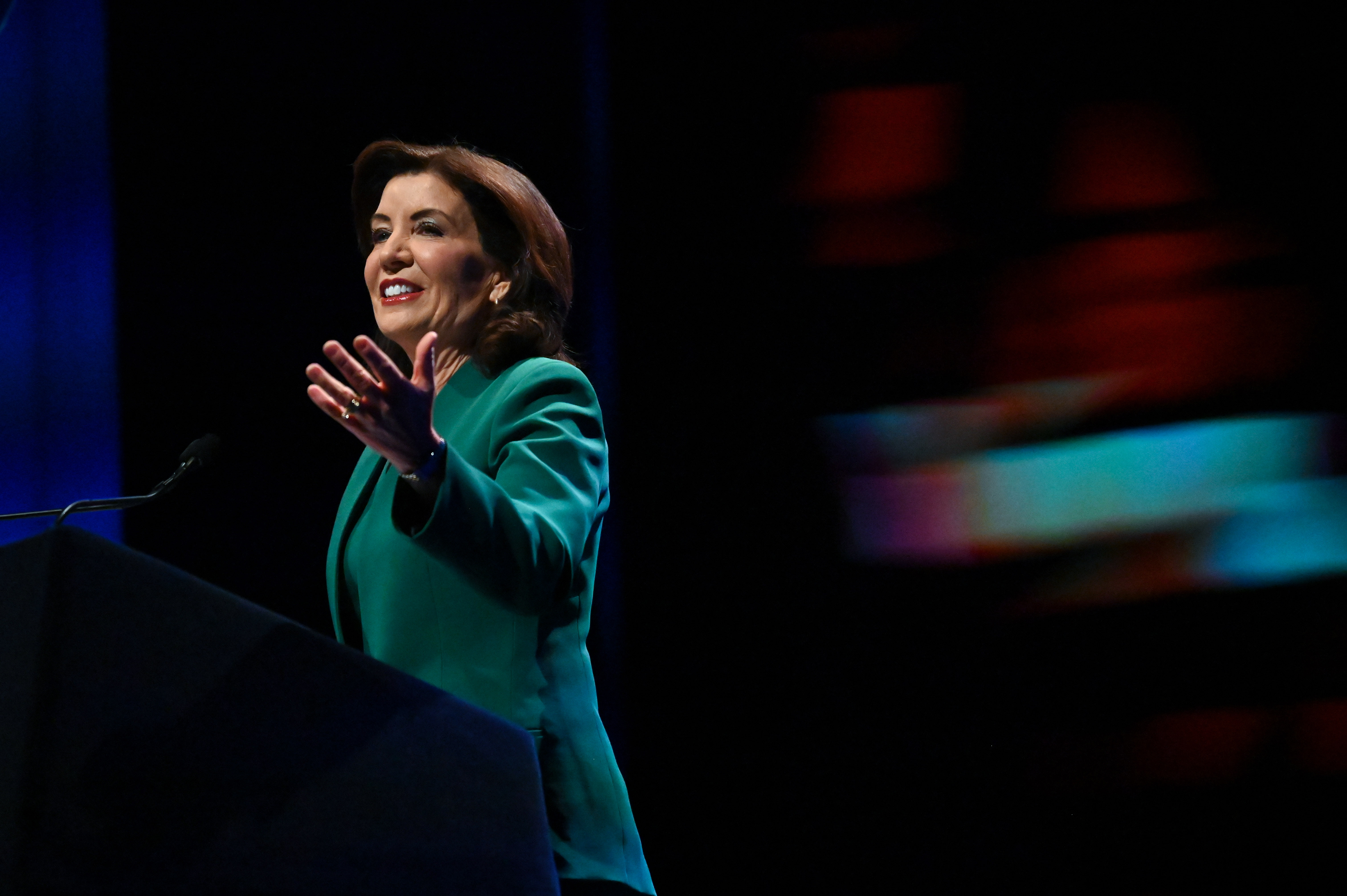 Gov. Kathy Hochul raises her hand at a podium.