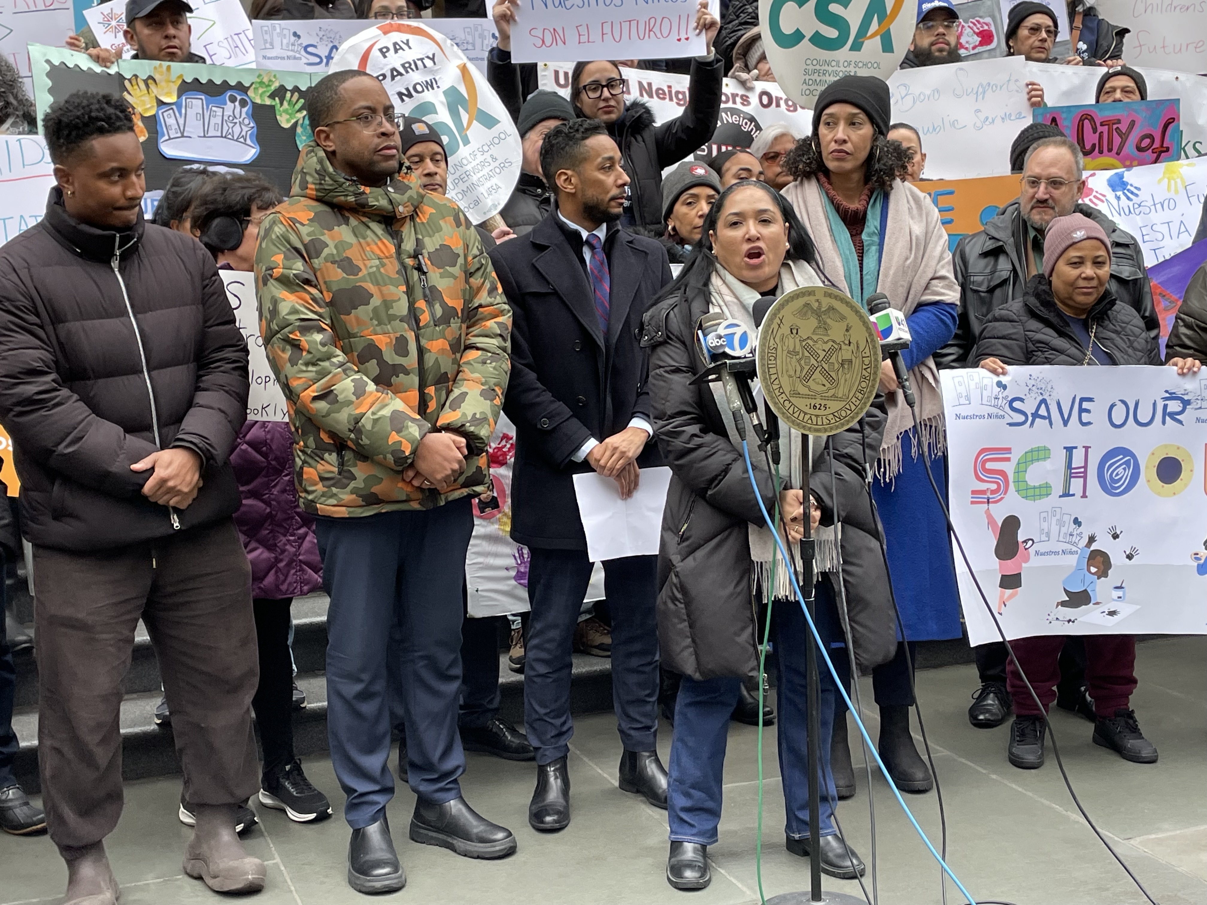 People stand at a podium outside in coats with signs.