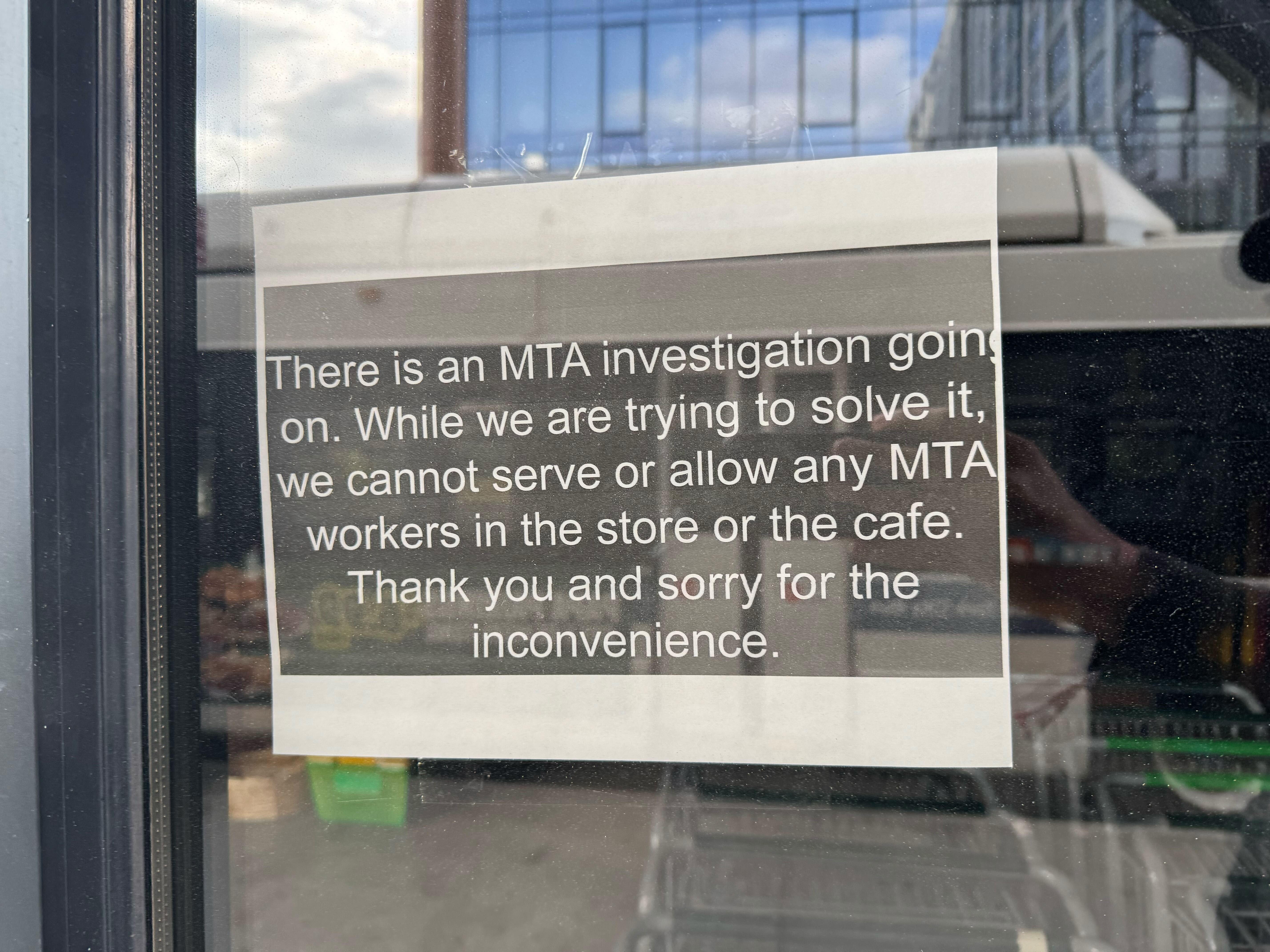 A sign at a grocery store window that says "There is an MTA investigation going on. While we try to solve it, we cannot serve or allow any MTA workers in the store or the cafe. Thank you and sorry for the inconvenience."