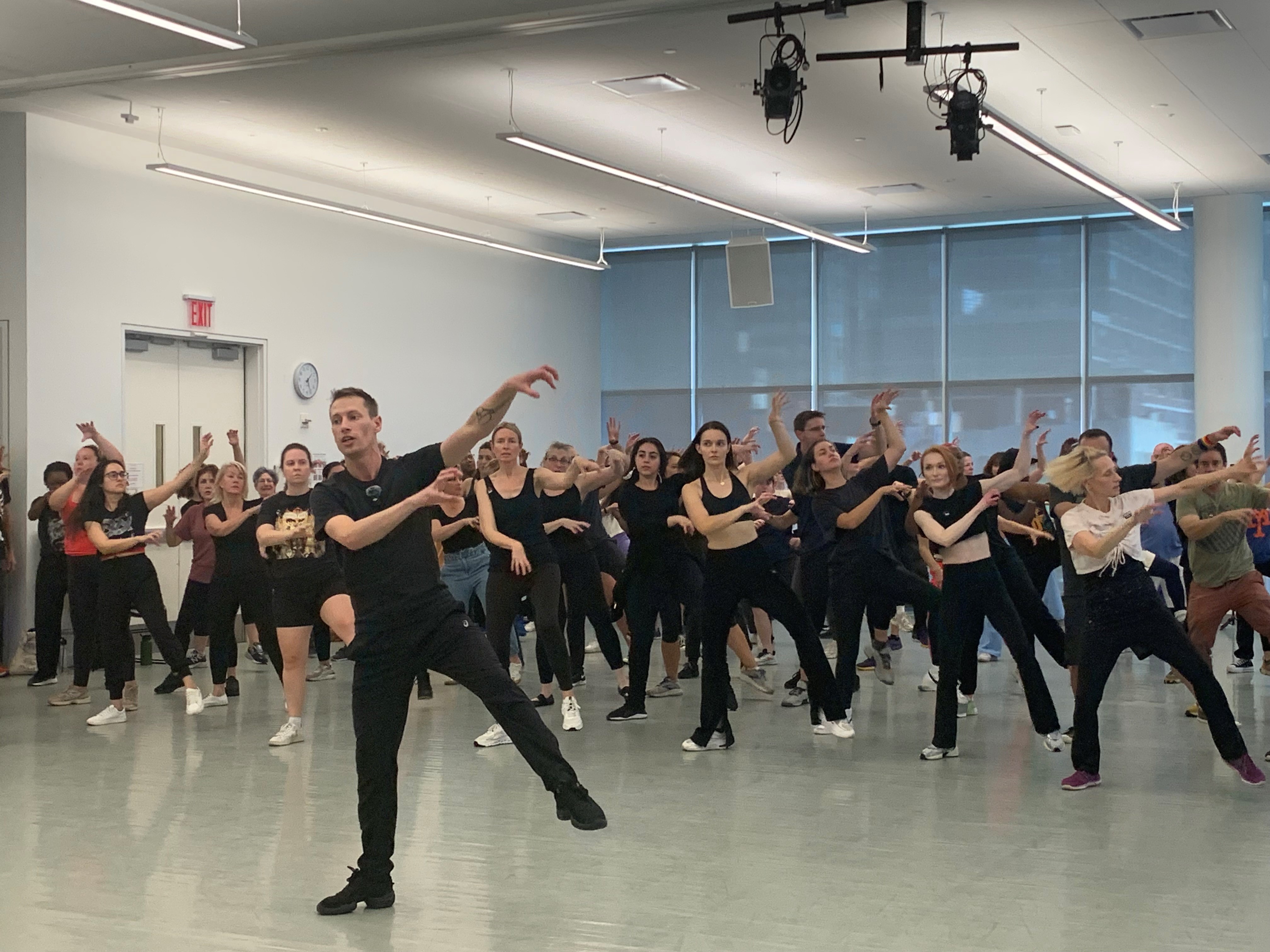 A group of people rehearses in a dance studio.