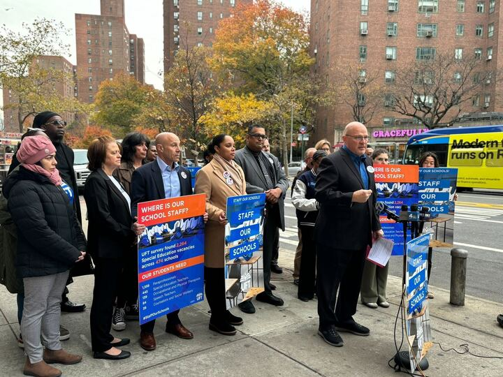 People on the street for a press conference holding signs that say "where is our school staff?"